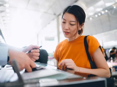 Eine Frau in einem orangenen Oberteil steht am Flughaftenschalter